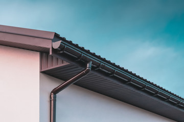 Chocolate-colored plastic gutter on the roof of the building and downpipe on the wall - obrazy, fototapety, plakaty