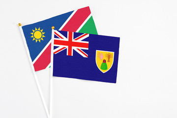Fototapeta premium Turks And Caicos Islands and Namibia stick flags on white background. High quality fabric, miniature national flag. Peaceful global concept.White floor for copy space.