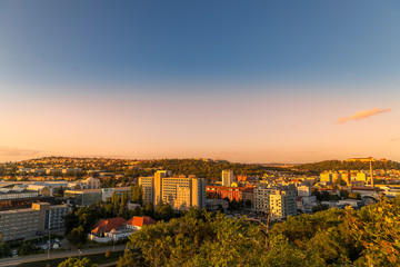 Fototapeta premium Sunset on Brno city part with exhibition center and apartments on a hill during orange sunset and public light turning online