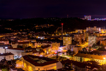 Crossing during late day to night timelapse to Mendel Square in Brno with cars and public transport, trams and buses passing through busy square and the surrounding streets which slowly light up.