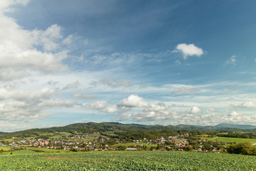 Fototapeta na wymiar Fast moving clouds in the sky captured during a sunny day overlooking the village and the high hills and mountains in the background foreground from a field with freshly sown crops.