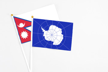 Antarctica and Nepal stick flags on white background. High quality fabric, miniature national flag. Peaceful global concept.White floor for copy space.