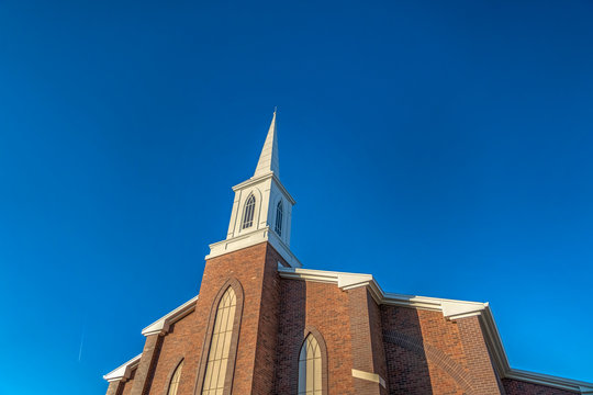Church with classic red brick exterior wall and white steeple against blue sky