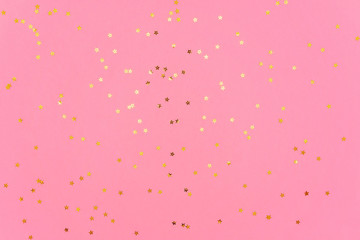 Photo of gold color stars glitter sprinkles on pink trendy background. Festive holiday background for your projects. Celebration concept. Christmas pattern. Top view, flat lay