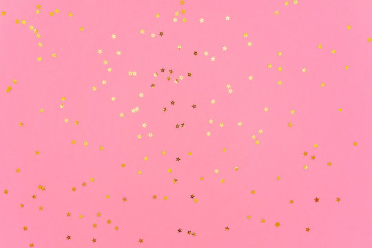 Photo of gold color stars glitter sprinkles on pink trendy background. Festive holiday background for your projects. Celebration concept. Christmas pattern. Top view, flat lay