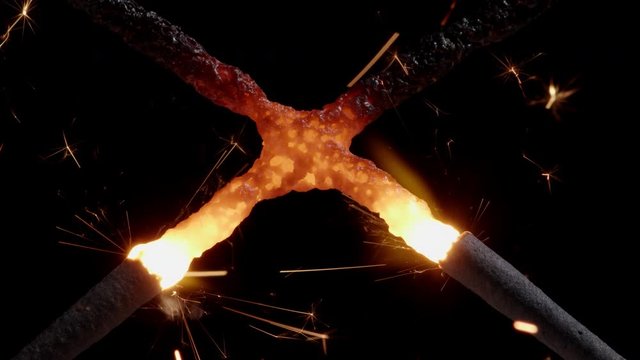 Macro shot of two crossed burning christmas sparklers releasing golden sparks and melting together while being forged into a red hot glowing cross.