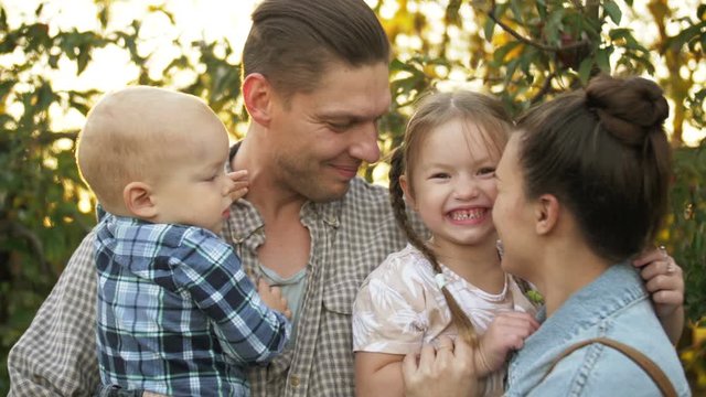 Happy father embracing his family in a Park on a Sunny day. Mom, dad and the little kids laughing and hugging at sunset in the Park.