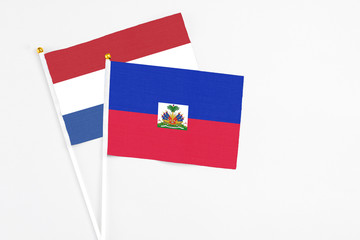 Haiti and Netherlands stick flags on white background. High quality fabric, miniature national flag. Peaceful global concept.White floor for copy space.