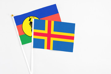 Aland Islands and New Caledonia stick flags on white background. High quality fabric, miniature national flag. Peaceful global concept.White floor for copy space.