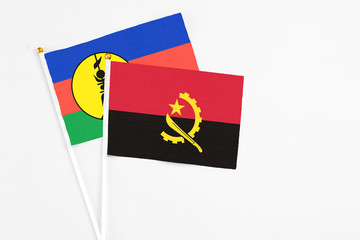 Angola and New Caledonia stick flags on white background. High quality fabric, miniature national flag. Peaceful global concept.White floor for copy space.