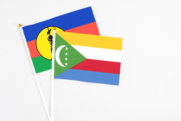 Comoros and New Caledonia stick flags on white background. High quality fabric, miniature national flag. Peaceful global concept.White floor for copy space.