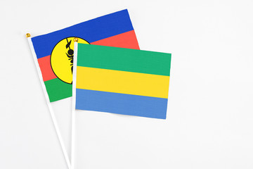 Gabon and New Caledonia stick flags on white background. High quality fabric, miniature national flag. Peaceful global concept.White floor for copy space.
