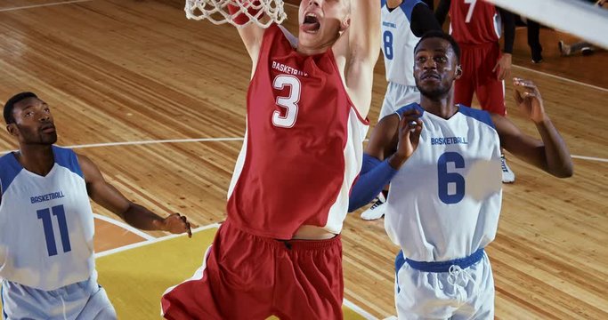 Professional basketball player in action performing slam dunk in a basketball hoop on a sports arena.