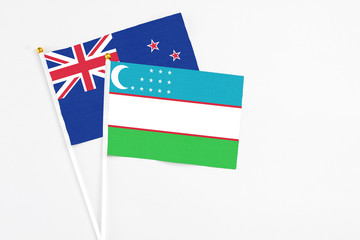 Naklejka premium Uzbekistan and New Zealand stick flags on white background. High quality fabric, miniature national flag. Peaceful global concept.White floor for copy space.