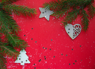 Christmas flatlay with green christmas tree branches and wood decorations on a red background 
