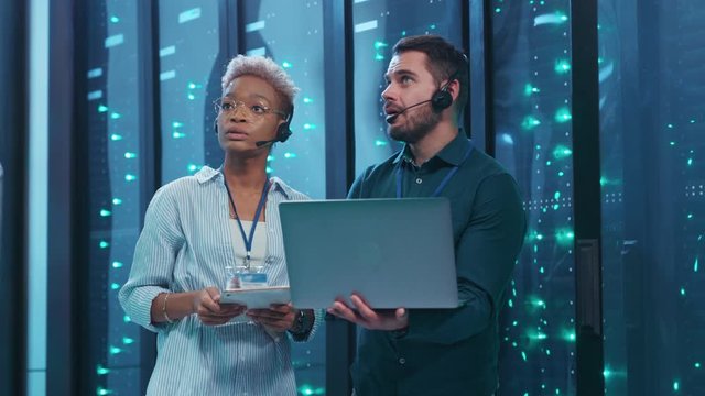 Multi-ethnic couple of server engineers inspecting supercomputer providing webhosting cloud computing coworking in data center security storage.