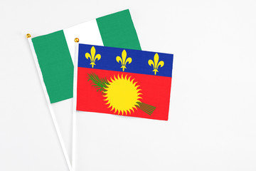 Guadeloupe and Nigeria stick flags on white background. High quality fabric, miniature national flag. Peaceful global concept.White floor for copy space.