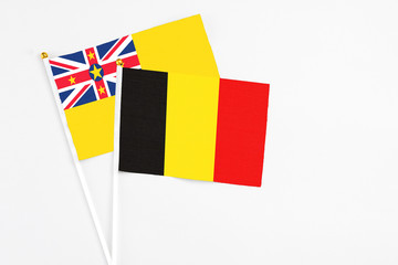 Naklejka premium Belgium and Niue stick flags on white background. High quality fabric, miniature national flag. Peaceful global concept.White floor for copy space.