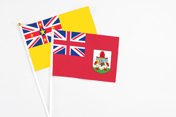 Fototapeta premium Bermuda and Niue stick flags on white background. High quality fabric, miniature national flag. Peaceful global concept.White floor for copy space.