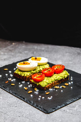 Healthy avocado toast with tomatoes and eggs for breakfast on a black plate