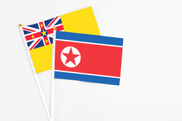North Korea and Niue stick flags on white background. High quality fabric, miniature national flag. Peaceful global concept.White floor for copy space.