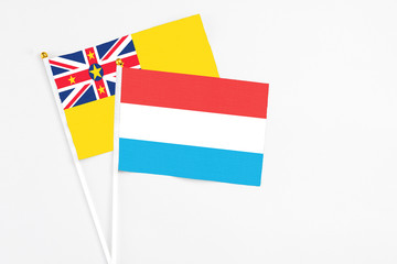 Luxembourg and Niue stick flags on white background. High quality fabric, miniature national flag. Peaceful global concept.White floor for copy space.