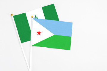 Djibouti and Norfolk Island stick flags on white background. High quality fabric, miniature national flag. Peaceful global concept.White floor for copy space.