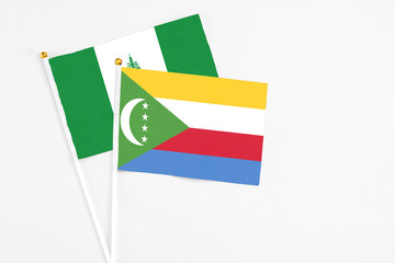 Comoros and Norfolk Island stick flags on white background. High quality fabric, miniature national flag. Peaceful global concept.White floor for copy space.