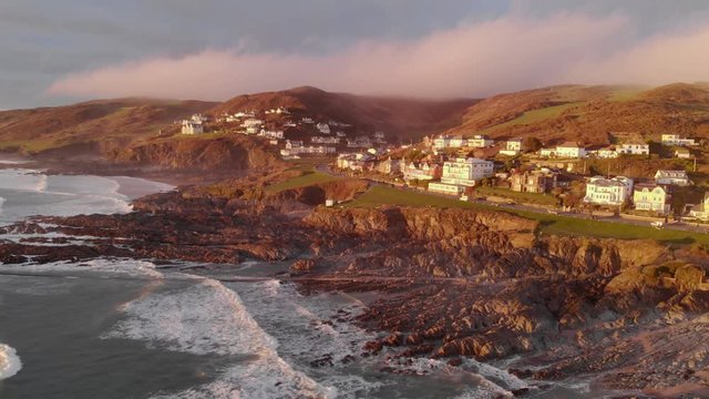 Aerial Landscape Woolacombe Village Rocky Coastline, Clouds Sitting Over Hills, Winter Sunset, Zooming Out And Panning Left