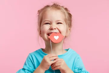 Fotobehang Funny smiley girl face on the background of a bright pink wall. Child girl with paper accessories, paper lips on a stick. © oes