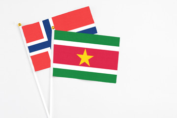 Suriname and Norway stick flags on white background. High quality fabric, miniature national flag. Peaceful global concept.White floor for copy space.