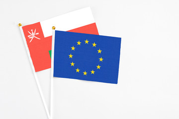 European Union and Oman stick flags on white background. High quality fabric, miniature national flag. Peaceful global concept.White floor for copy space.