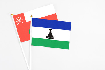 Lesotho and Oman stick flags on white background. High quality fabric, miniature national flag. Peaceful global concept.White floor for copy space.