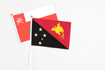 Papua New Guinea and Oman stick flags on white background. High quality fabric, miniature national flag. Peaceful global concept.White floor for copy space.