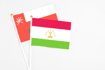 Tajikistan and Oman stick flags on white background. High quality fabric, miniature national flag. Peaceful global concept.White floor for copy space.
