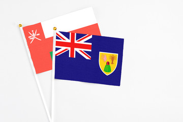 Fototapeta premium Turks And Caicos Islands and Oman stick flags on white background. High quality fabric, miniature national flag. Peaceful global concept.White floor for copy space.