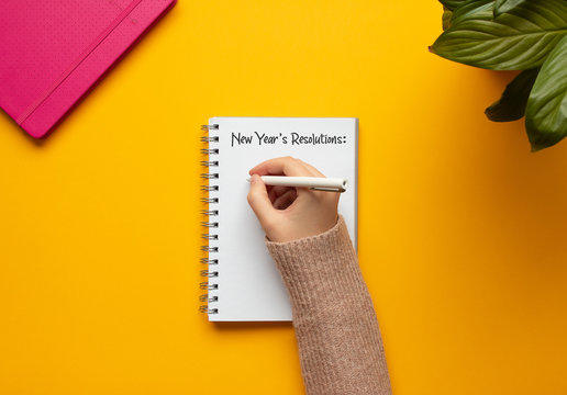 Stock Photo Of A Young Woman Hand Writing In A 2020 New Year Notebook With List Of Resolutions And Objects On Yellow Background