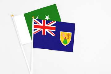 Fototapeta premium Turks And Caicos Islands and Pakistan stick flags on white background. High quality fabric, miniature national flag. Peaceful global concept.White floor for copy space.