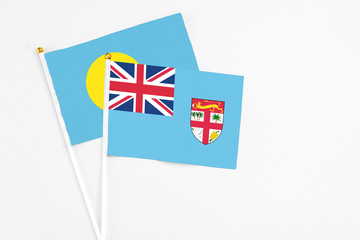 Fototapeta premium Fiji and Palau stick flags on white background. High quality fabric, miniature national flag. Peaceful global concept.White floor for copy space.