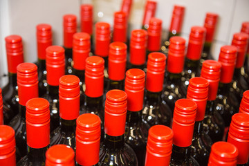 Metal corks of bright red color on glass bottles in rows. Drinks, food, design, structures.