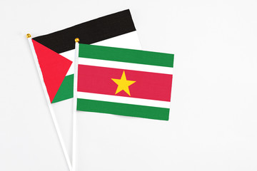 Suriname and Palestine stick flags on white background. High quality fabric, miniature national flag. Peaceful global concept.White floor for copy space.