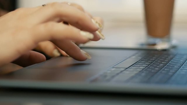 Close-up of female hands using touchpad and surfing internet, modern student works on a laptop while sitting in cafe