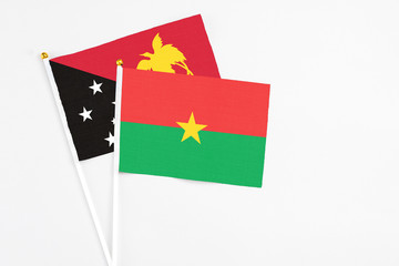Burkina Faso and Papua New Guinea stick flags on white background. High quality fabric, miniature national flag. Peaceful global concept.White floor for copy space.