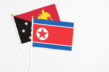 North Korea and Papua New Guinea stick flags on white background. High quality fabric, miniature national flag. Peaceful global concept.White floor for copy space.