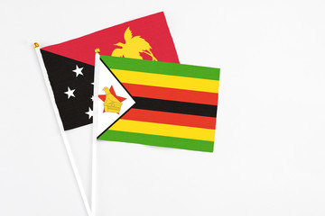 Zimbabwe and Papua New Guinea stick flags on white background. High quality fabric, miniature national flag. Peaceful global concept.White floor for copy space.