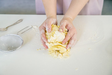 Woman's hands knead dough on a white table