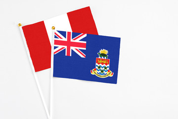Fototapeta premium Cayman Islands and Peru stick flags on white background. High quality fabric, miniature national flag. Peaceful global concept.White floor for copy space.