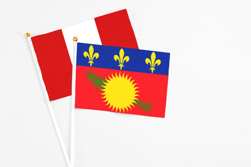 Guadeloupe and Peru stick flags on white background. High quality fabric, miniature national flag. Peaceful global concept.White floor for copy space.