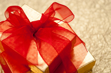 Two gold gift boxes with red ribbons stacked on textured metallic gold background with copy space