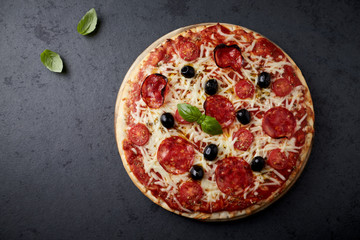 Pizza with chorizo, mozzarella cheese, cherry tomatoes, black olives and oregano. Home made food. Concept for a tasty and hearty meal. Black stone background. Top view. 